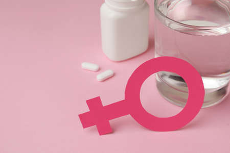 Female gender sign, pills and glass of water on pink background, closeup. Space for textの写真素材