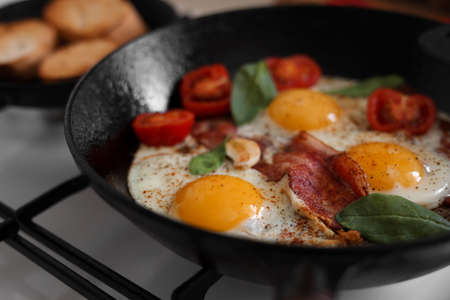 Delicious fried eggs with bacon and tomatoes in pan, closeupの写真素材