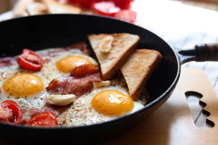 Delicious fried eggs with bacon and tomatoes in pan, closeupの写真素材