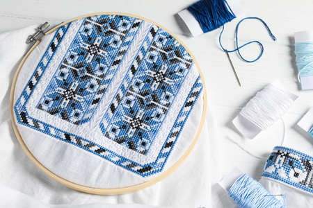Shirt with blue embroidery design in hoop, needle and threads on white wooden table, flat lay. National Ukrainian clothesの写真素材