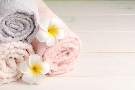 Closeup view of soft folded towels and plumeria flowers on white wooden table, space for textの写真素材