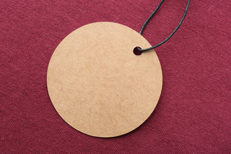 Circle shaped tag with space for text on dark red fabric, top viewの写真素材