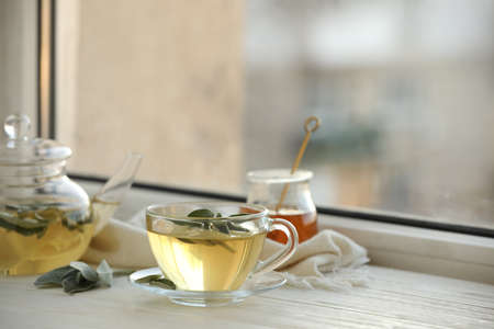 Cup of sage tea and green leaves on white wooden windowsill. Space for textの写真素材