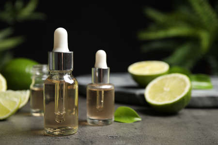 Lime essential oil and cut citrus fruits on gray table. Space for textの写真素材