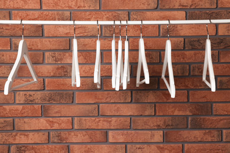 White clothes hangers on rail near red brick wall. Space for textの写真素材