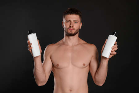 Shirtless young man holding bottles of shampoo on black backgroundの写真素材