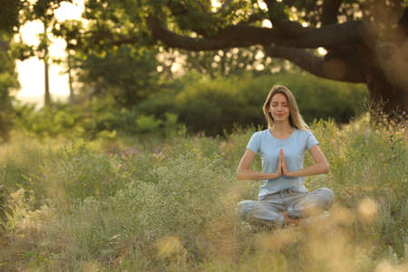 Young woman meditating on green grass in park, space for textの写真素材