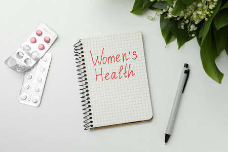 Notebook with text Women's Health and pills on white table, flat layの写真素材