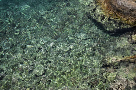 Shallow water with rocky sea bottom as background, top view