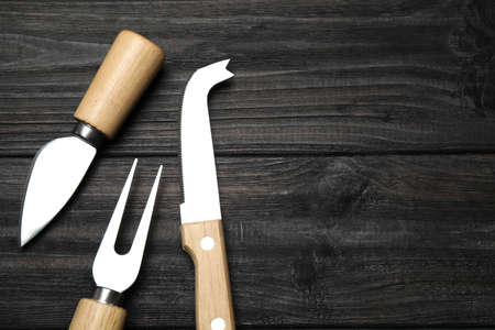 Cheese knives and fork on black wooden table, flat lay. Space for textの写真素材