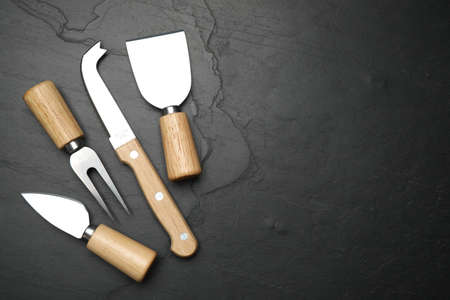 Cheese knives and fork on black stone table, flat lay. Space for text