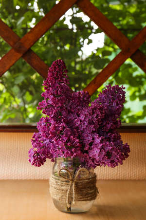 Beautiful lilac flowers in glass jar on wooden table indoors