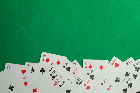 Scattered playing cards on green table, top view. Space for text