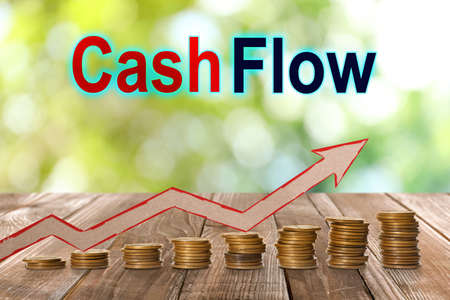 Cash flow concept. Illustration of upward arrow and stacked coins on wooden table against blurred green backgroundの写真素材