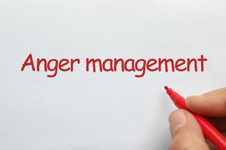 Man writing phrase Anger Management with red felt tip pen on white paper, top viewの写真素材