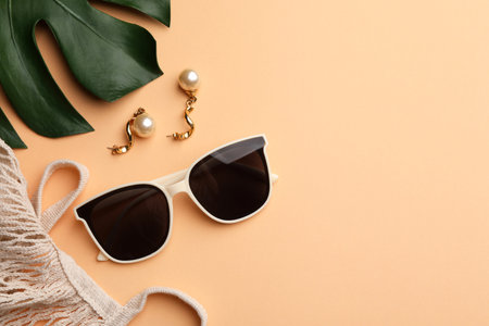 New stylish elegant sunglasses, beautiful earrings and bag on beige background, flat lay. Space for textの写真素材
