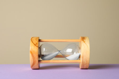 Hourglass with sand on violet table against beige background. menopause concept