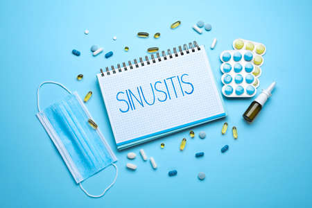 Notebook with word SINUSITIS, medical mask and different drugs on light blue background, flat lay