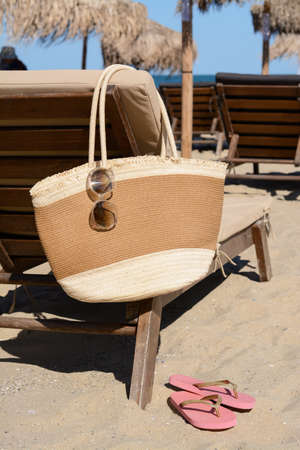Straw bag with sunglasses on wooden sunbed near sea. beach accessoriesの写真素材