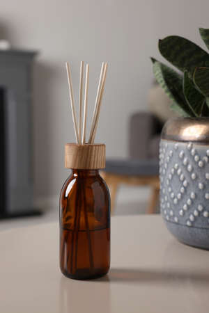 Aromatic reed air freshener near houseplant on light table indoorsの写真素材