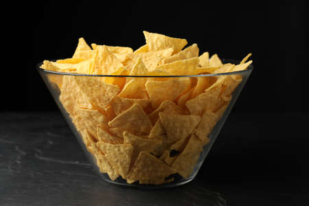 Glass bowl with tortilla chips (nachos) on black table against dark backgroundの写真素材