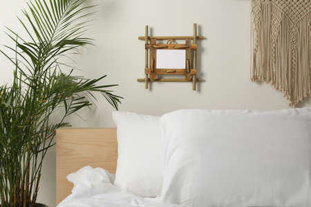 Empty bamboo frame hanging on white wall in bedroomの写真素材