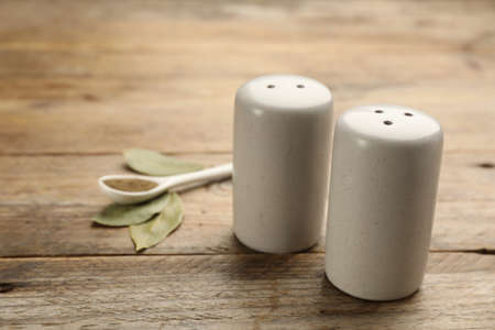 Ceramic salt and pepper shakers, bay leaves with spoon on wooden table, closeupの写真素材