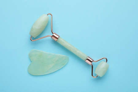 Jade gua sha tool and facial roller on light blue background, flat lay