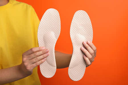 Woman holding beige orthopedic insoles on orange background, closeupの写真素材