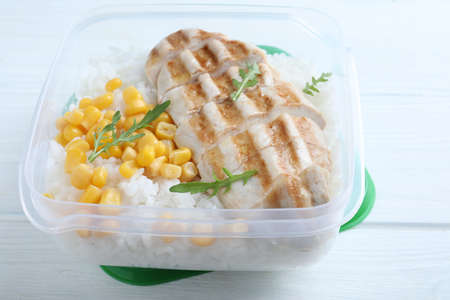 Tasty rice with grilled meat and corn in plastic container on white wooden table, closeupの写真素材