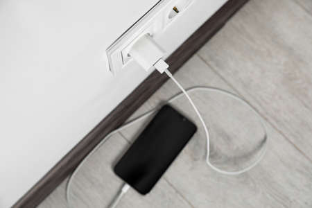 Modern smartphone charging from electric socket indoors, above viewの写真素材