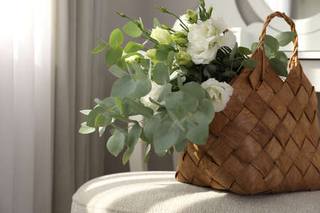 Stylish wicker basket with bouquet of flowers on ottoman in roomの写真素材