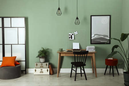 Typewriter, stack of papers and mood board on wooden table near pale green wall. Writer's workplaceの写真素材