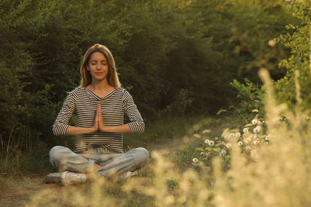 Young woman meditating on green grass outdoors, space for text