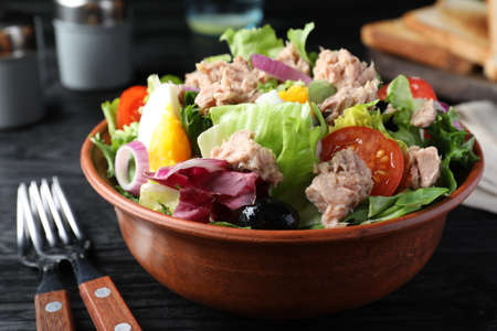 Bowl of delicious salad with canned tuna and vegetables served on black wooden table, closeupの写真素材