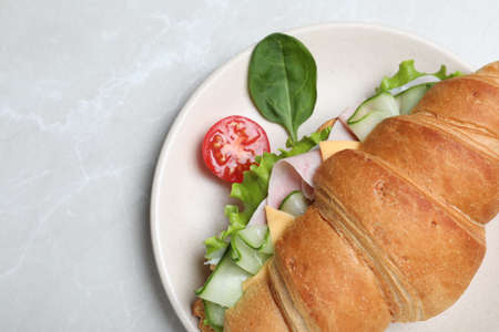 Tasty croissant sandwich with ham and cucumber on light gray marble table, top viewの写真素材
