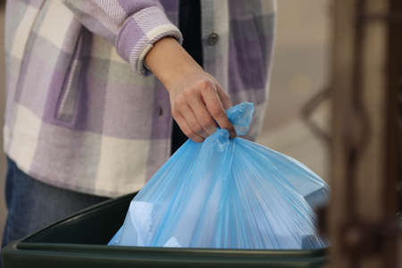 Woman putting garbage bag into recycling bin outdoors, closeupの写真素材