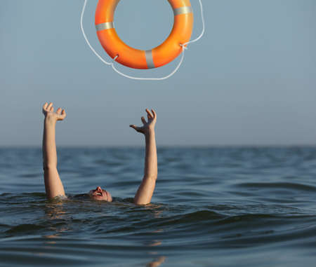 Drowning woman with raised hands getting lifebelt in sea
