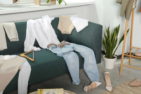 Messy pile of clothes on sofa and shoes in living roomの写真素材