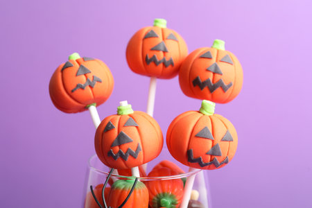 Delicious pumpkin shaped cake pops on violet background, closeup. Halloween treatmentの写真素材