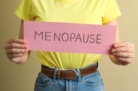 Woman holding card with word Menopause on beige background, closeupの写真素材