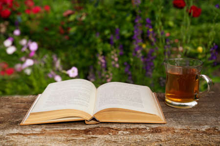 Open book with glass cup of tea on wooden table in gardenの写真素材