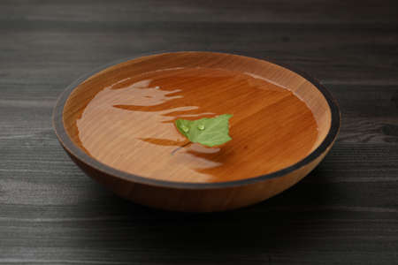 Bowl with water and green leaf on dark wooden table, closeupの写真素材