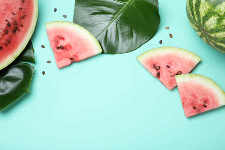 Delicious ripe watermelon and tropical leaves on turquoise background, flat lay. Space for text