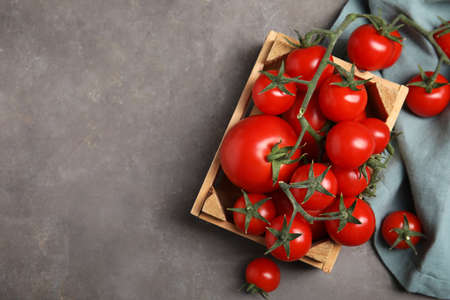 Many ripe red tomatoes in wooden crate on gray table, flat lay. Space for textの写真素材