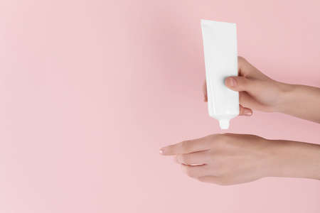 Woman applying cream onto hand on pink background, closeup. Space for textの写真素材