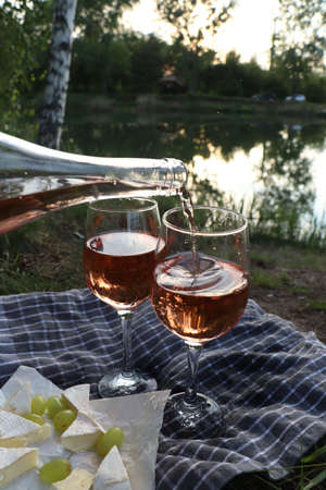 Pouring delicious rose wine into glass on picnic blanket near lake, closeupの写真素材