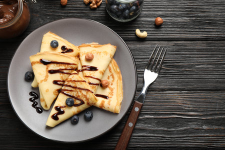 Delicious thin pancakes with chocolate, blueberries and nuts on black wooden table, flat layの写真素材