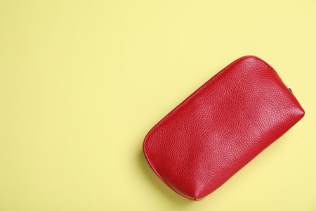 Red leather cosmetic bag on yellow background, top view. Space for text
