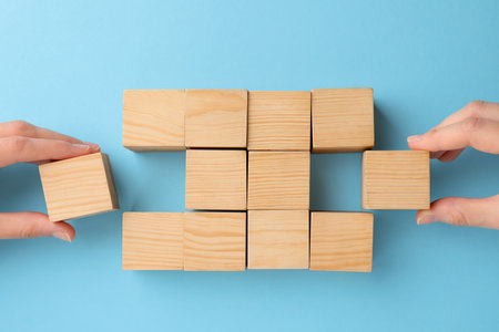 People holding wooden cubes near others on light blue background, top view. management concept